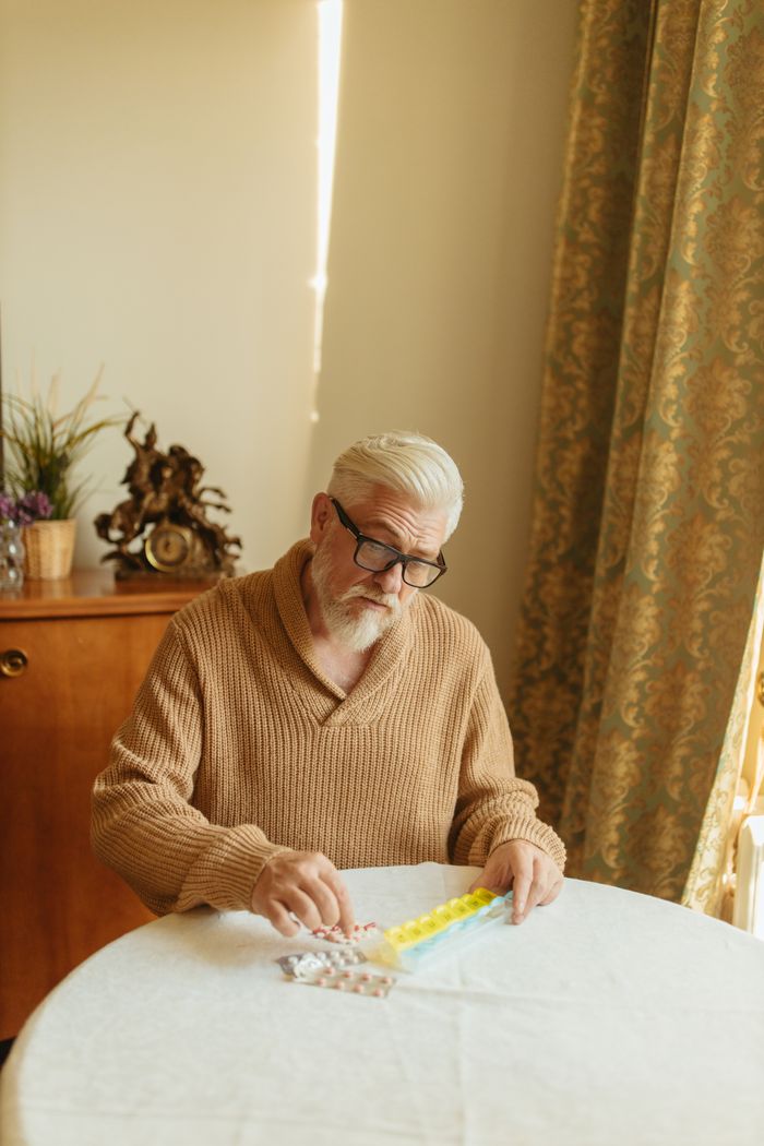 about-01 Elderly man with glasses arranging pills in a daily organizer at home.